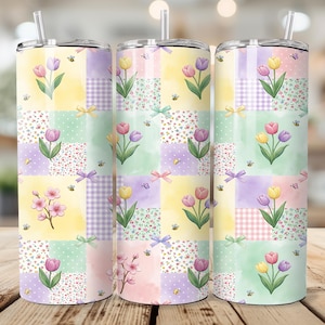 Könnte beinhalten: Drei Edelstahlbecher mit Blumen- und Patchwork-Designs. Jeder Becher hat ein farbenfrohes Patchworkmuster mit Tulpen, Bienen und Schleifen. Die Becher haben einen Strohhalm und stehen auf einer Holzoberfläche.