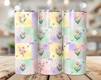 May include: Three stainless steel tumblers with floral and patchwork designs. Each tumbler features a colorful patchwork pattern with tulips, bees, and bows. The tumblers have a straw and are set on a wooden surface.