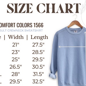 Puede incluir: Una sudadera de cuello redondo azul claro para adultos en una percha, con una tabla de tallas. La tabla enumera las tallas S a 3XL, con las medidas correspondientes de ancho y largo en cent&iacute;metros. El texto dice "COMFORT COLORS 1566".