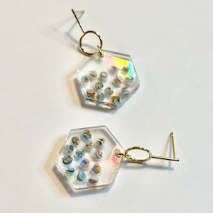 May include: A pair of hexagonal earrings with a clear resin base and a gold-toned hook. The resin contains small, colorful, swirling marbles.