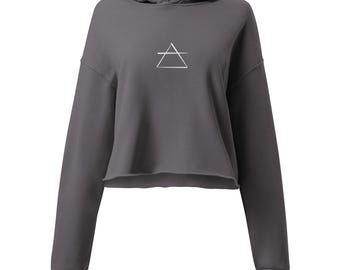 Puede incluir: Una sudadera con capucha corta de color gris carbón con capucha con cordón y mangas largas. Un símbolo geométrico blanco está centrado en el pecho. El dobladillo inferior no está terminado.