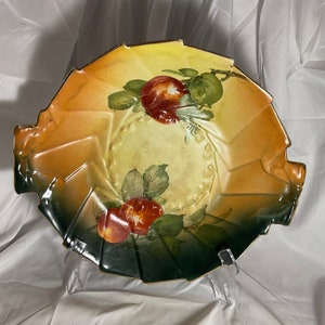 May include: A vintage ceramic bowl with a scalloped edge and a green, yellow, and orange glaze. The bowl features a painted design of apples and leaves.