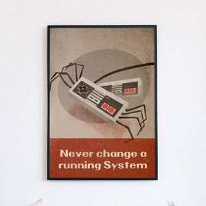 Könnte beinhalten: Ein Vintage-Poster mit braunem Hintergrund, auf dem zwei Retro-Videospielcontroller mit schwarzen Kabeln zu sehen sind. Die Controller sind als Spinne mit acht Beinen dargestellt. Der Text "Ändere niemals ein laufendes System" ist in Weiß auf rotem Hintergrund gedruckt.