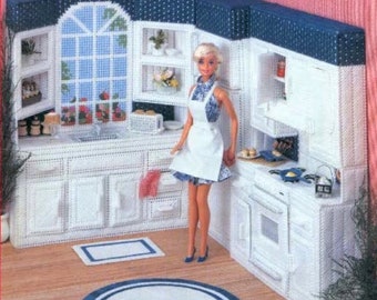 Puede incluir: Un juego de cocina de casa de muñecas blanca con una muñeca de pie delante. La cocina tiene un fregadero, armarios, una estufa y un horno. La muñeca lleva un vestido blanco con un estampado azul y blanco.