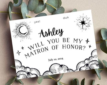 May include: A white card with black text and illustrations. The text reads "yes! duh Ashley WILL YOU BE MY MATRON OF HONOR? July 10, 2024". The illustrations include a crescent moon, a star, and clouds.