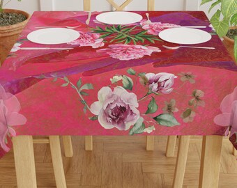 May include: A rectangular tablecloth with a vibrant pink and red floral design. The tablecloth features a watercolor-style pattern of peonies and other flowers, with white plates and silverware set on top. The table is surrounded by wooden chairs.