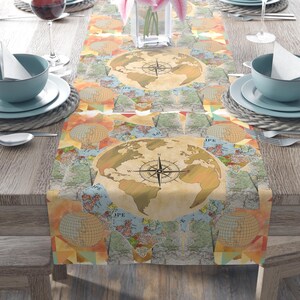 May include: A table runner with a vintage world map design. The runner features a large globe with a compass rose in the center, surrounded by smaller map details. The color palette includes beige, blue, and orange tones, creating a classic, travel-themed aesthetic.