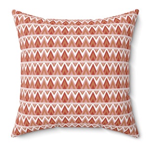 May include: A decorative throw pillow with a geometric pattern of red, orange, and pink triangles on a white background.