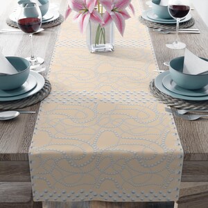 May include: A beige table runner with a pearl and chain design. The runner is on a wooden table with two place settings on each side.