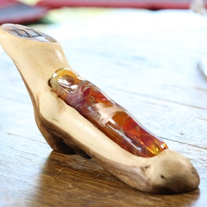 May include: A wooden stand with a carved out space to hold a small, colorful glass bottle. The bottle is filled with a swirling mix of orange, red, and white glass.