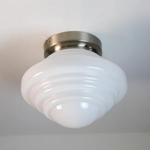 Op de afbeelding: Een witte plafondlamp met een zilveren metalen basis en een gelaagde glazen kap.