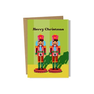 May include: A Christmas card featuring two colorful nutcracker figures. The nutcrackers have red and gold uniforms, blue hair, and are standing on a green and yellow background. The words "Merry Christmas" are at the top.
