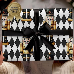 May include: Gift wrapped in paper with a black and white diamond pattern and nutcracker soldiers. A black ribbon is tied around the gift. The paper has a gold sticker that says "Premium Wrapping Paper".
