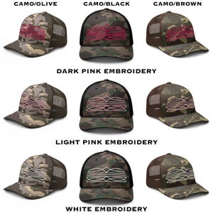 May include: A collection of camouflage baseball caps with mesh backs. The caps feature embroidered designs in various colors, including pink and white, and are available in camo/olive, camo/black, and camo/brown.