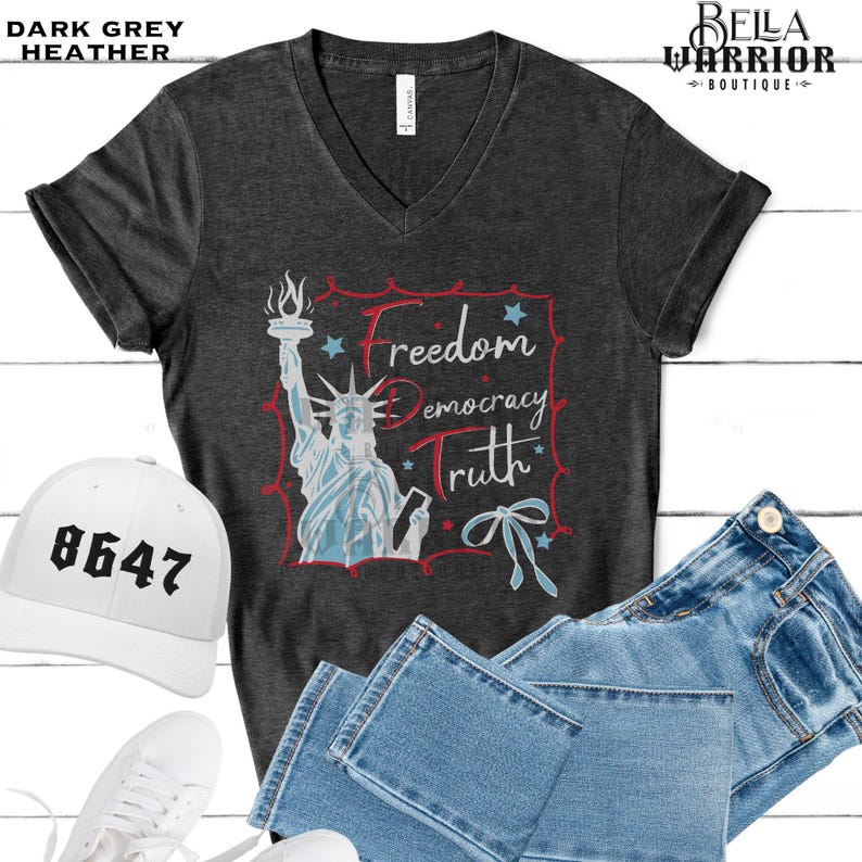 May include: Dark grey heather v-neck t-shirt with a graphic of the Statue of Liberty and the words "Freedom, Democracy, Truth". A white baseball cap with the number "8647" is also visible.