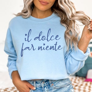 K&ouml;nnte beinhalten: Ein hellblaues Sweatshirt mit dem Text "il dolce far niente" in blauer Schrift.