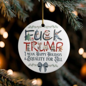 Può includere: Ornamento natalizio rotondo bianco con la scritta "FUCK TRUMP" in rosso e blu, con illustrazioni a tema festivo. L'ornamento include anche la scritta "I MEAN, HAPPY HOLIDAYS & EQUALITY FOR ALL."