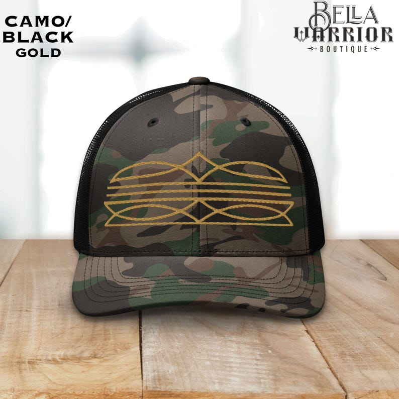 May include: Camo trucker hat with a black mesh back and a gold embroidered design. The hat features the text "CAMO/ BLACK GOLD" on the front and the "BELLA WARRIOR BOUTIQUE" logo on the side.