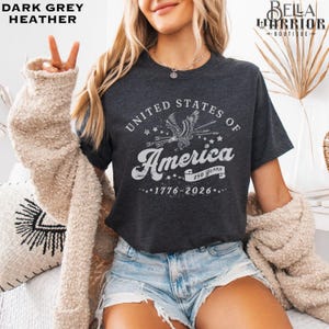 Puede incluir: Camiseta gris oscuro jaspeado con el texto "United States of America" y un gr&aacute;fico de &aacute;guila. La camiseta tambi&eacute;n presenta el texto "250 Years" y "1776-2026".