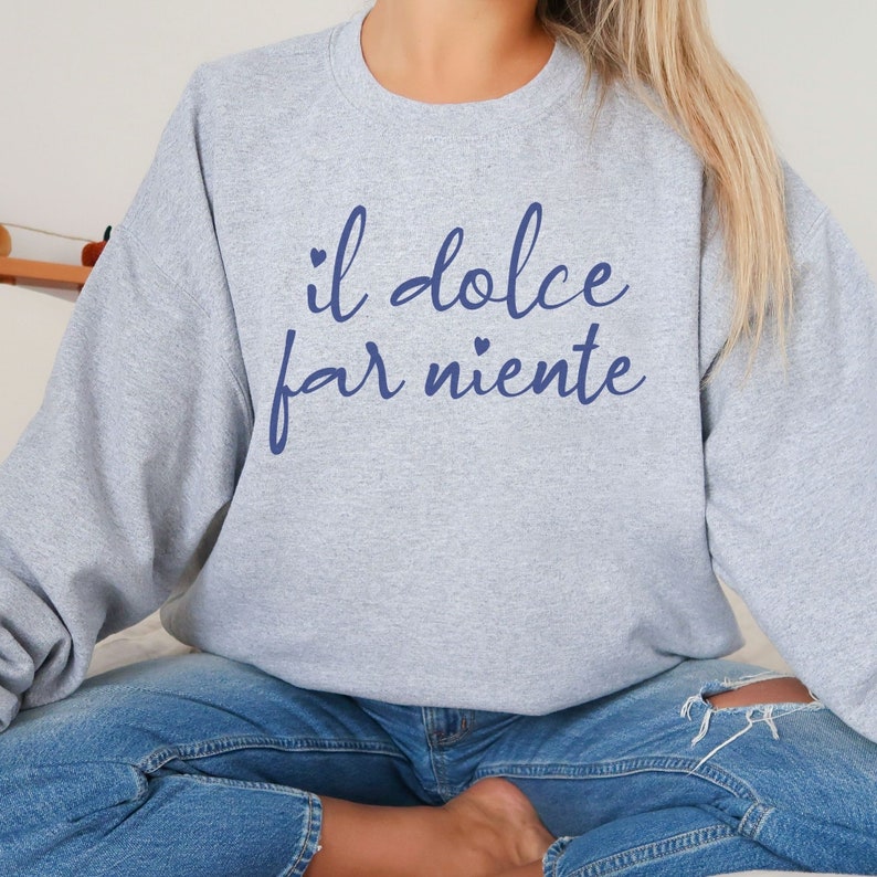 K&ouml;nnte beinhalten: Grauer Pullover mit dem Text "il dolce far niente" in blauer Schrift mit kleinen Herzen auf beiden Seiten des Textes.