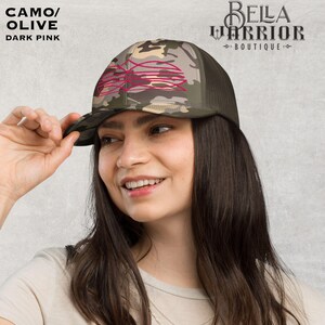 May include: Camo/Olive trucker hat with a dark pink design. The hat features a camouflage pattern on the front panel and a mesh back. The text "CAMO/OLIVE" and "DARK PINK" is visible on the top left. The Bella Warrior Boutique logo is on the top right.