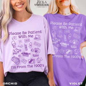 Puede incluir: Una camiseta de color violeta claro y una camiseta de color violeta, ambas con el texto "Please Be Patient With Me I'm From The 1900's" y varias ilustraciones de l&iacute;nea de objetos vintage como un reproductor de casetes, patines y televisi&oacute;n.