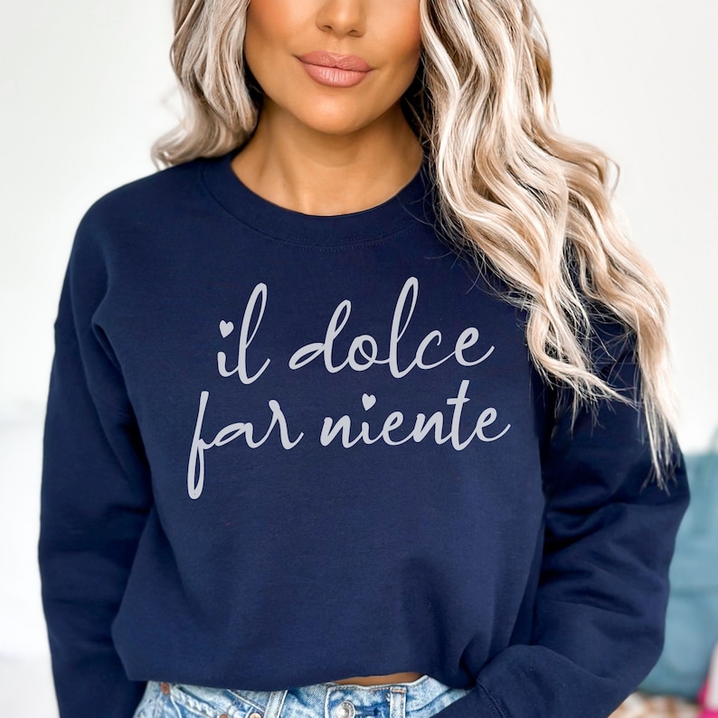 K&ouml;nnte beinhalten: Ein marineblauer Pullover mit dem Text "il dolce far niente" in wei&szlig;en Buchstaben.