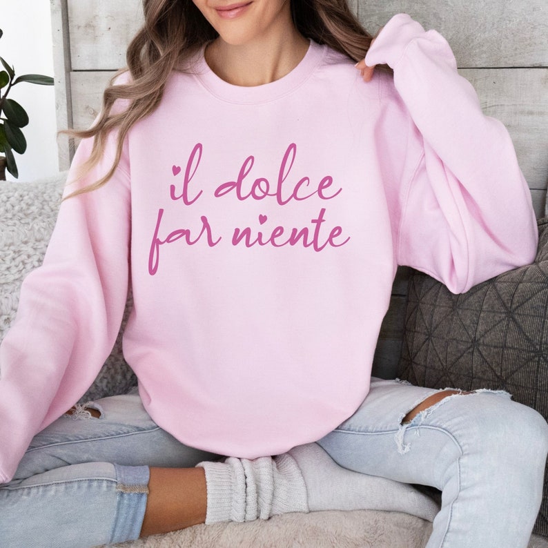 K&ouml;nnte beinhalten: Rosafarbener Pullover mit dem Text "il dolce far niente" in rosafarbener Schrift.