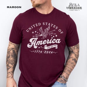 Puede incluir: Camiseta granate con el texto blanco "UNITED STATES OF America", un gr&aacute;fico de &aacute;guila y las fechas "1776-2026". La camiseta tambi&eacute;n tiene el texto "250 YEARS". La palabra "MAROON" est&aacute; en la esquina superior izquierda.