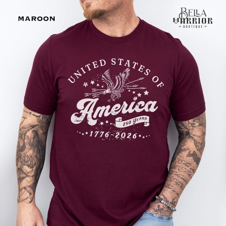 Puede incluir: Camiseta granate con el texto blanco "UNITED STATES OF America", un gr&aacute;fico de &aacute;guila y las fechas "1776-2026". La camiseta tambi&eacute;n tiene el texto "250 YEARS". La palabra "MAROON" est&aacute; en la esquina superior izquierda.