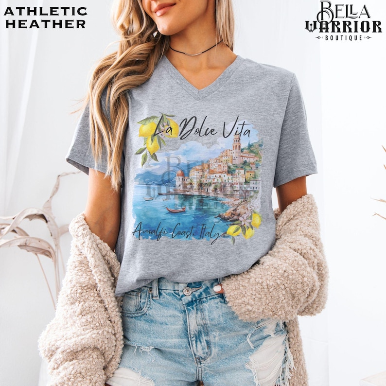 May include: Grey V-neck t-shirt with a watercolour illustration of a coastal Italian town with the text "La Dolce Vita" and "Amalfi Coast, Italy".
