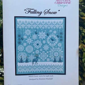 May include: A printed pattern titled "Falling Snow" with a winter theme. The design features snowflakes, a deer, and pine trees in shades of white and blue. The text includes the designer's name and stitch count.