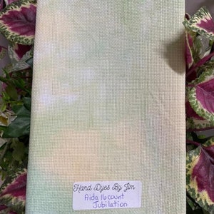 May include: Aida fabric hand-dyed in shades of green, yellow, and white. The fabric is labeled "Hand Dyes By Jim" and "Aida 18 count Jubilation".