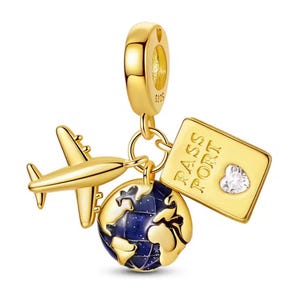 May include: Gold-coloured travel charm featuring a plane, passport, and globe. The passport reads "PASS PORT" and has a heart-shaped gem. The globe has a blue and gold design. The charm hangs from a gold loop.