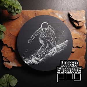 Puede incluir: Una placa circular de madera negra con una silueta blanca de un snowboarder en el aire, con un fondo nevado. El texto "LASER ENGRAVE PRO" est&aacute; impreso en blanco en la parte inferior de la placa.
