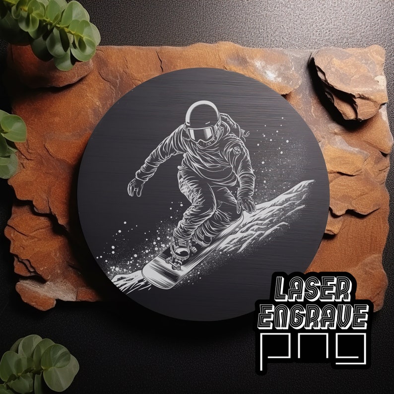 Puede incluir: Una placa circular de madera negra con una silueta blanca de un snowboarder en el aire, con un fondo nevado. El texto "LASER ENGRAVE PRO" est&aacute; impreso en blanco en la parte inferior de la placa.