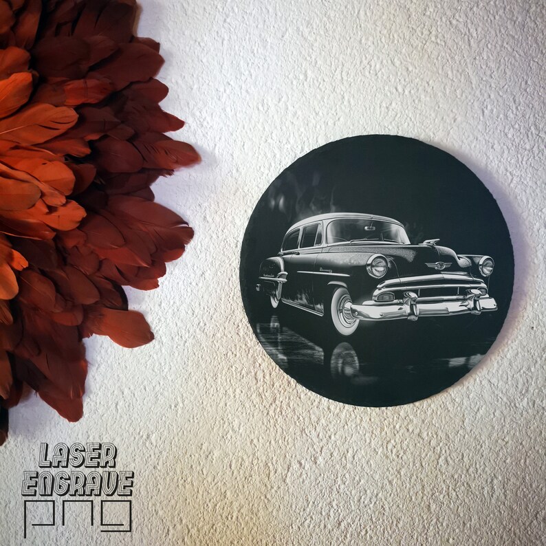 May include: A black and white laser engraved image of a vintage car on a round black slate coaster.