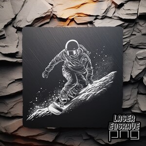 Puede incluir: Una ilustraci&oacute;n en blanco y negro de un snowboarder en el aire, con una monta&ntilde;a nevada en el fondo. La imagen est&aacute; grabada en una baldosa de pizarra negra con el texto "Laser Engrave Pro" en la esquina inferior derecha.