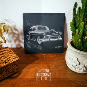 May include: Black and white laser engraved image of a vintage car on a black slate tile. The car is a 1950s Chevrolet with a chrome bumper and grill. The image is set against a dark background.