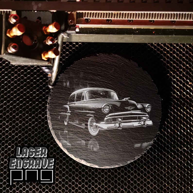 May include: A black and white laser engraved image of a vintage car on a round black slate coaster.