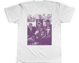 May include: A white t-shirt featuring a purple print of three people standing in front of a sign that reads "Reserved for Blink". The sign has a wheelchair symbol on it.