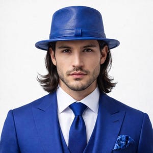 May include: A vibrant blue fedora hat with a matching band sits atop a man's head. He is wearing a blue suit, white dress shirt, and blue tie. A blue patterned pocket square is visible.