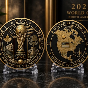 May include: Two-sided gold-colored commemorative coin for the 2026 World Cup. One side features the trophy, flags, and text "USA, Canada, Mexico, Three Nations, One Champion." The other side shows a map of North America with the text "United by Passion, Inspired by Football."