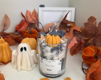 Puede incluir: Una vela en frasco de vidrio transparente con cera blanca y gris en espiral, decorada con una pequeña calabaza naranja y un sombrero de bruja gris. La etiqueta dice La Belle Lumiere London, Spooky Night y Happy Halloween.