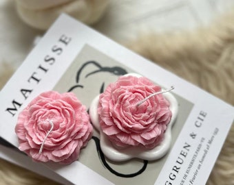 Puede incluir: Dos velas de color rosa en forma de flor con mechas blancas sobre un fondo blanco. Las velas están sobre una tarjeta con el texto "MATISSE" y "BERGGRUEN & CIE" en negro.