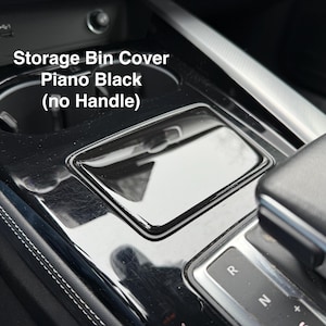 Puede incluir: Primer plano de la consola central de un coche con una tapa de guantera negra piano. La tapa es rectangular y tiene un acabado brillante. El texto "Storage Bin Cover Piano Black (no Handle)" es visible.