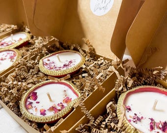 Puede incluir: Velas en soportes decorativos con adornos dorados y pétalos de rosa secos, dentro de una caja de cartón con papel triturado. La caja tiene una pegatina que dice "Happy Diwali".