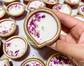 May include: A collection of small, decorative candles in red and gold holders. Each candle has a white wax base, adorned with dried rose petals. The holders have a gold rim and a unique shape, creating an elegant and festive look.
