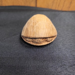Peut inclure: Une petite figurine de tortue en bois avec une carapace détaillée et un visage sculpté. La tortue est refermée, avec sa tête et ses pattes rentrées dans la carapace.