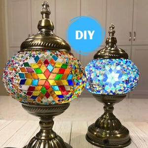 May include: Two decorative mosaic lamps with ornate bronze bases. One lamp features a colorful mosaic design with red, yellow, green, and blue glass. The other lamp has a blue and white mosaic pattern. The word "DIY" is in a blue circle.
